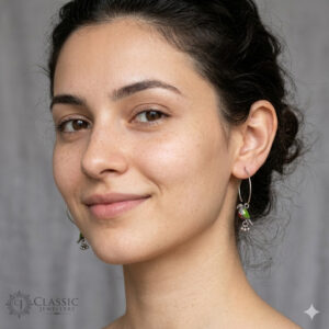 A detailed pair of large, thin-wire German silver hoop earrings featuring hanging detailed green and red enamel parrot charms with small silver berry dangles.