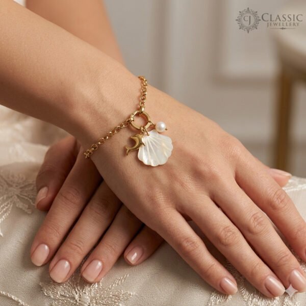 A gold-plated chain charm bracelet featuring a carved golden dolphin, a white mother-of-pearl shell, and a small pearl accent.