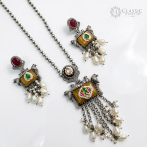 A matching set of vintage-style oxidized silver-tone jewelry, including a pendant necklace and two drop earrings, featuring pink rectangular quartz, green emerald studs, multi-colored gemstone embellishments, and white pearl clusters, shown against a white background.