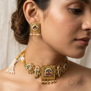 Model wearing a detailed gold choker necklace with blue, red, green gems and pearl dangles, with matching stud earrings. Kreezo Collection logo visible.