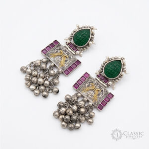 German silver dangle earrings featuring a large green teardrop stone, golden bird motifs, magenta accents, and silver ghungroo dangles.