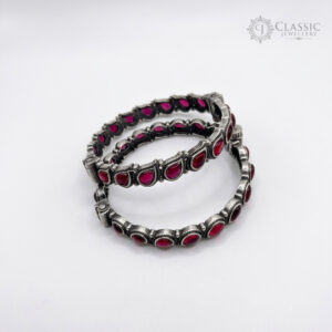 A pair of handcrafted german silver bangles studded with vibrant red teardrop and oval stones.