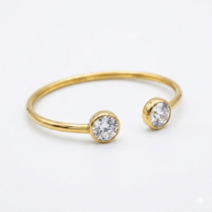 A slim, polished gold open-cuff kada featuring two round-cut bezel-set clear crystals on each end, displayed on a white background.