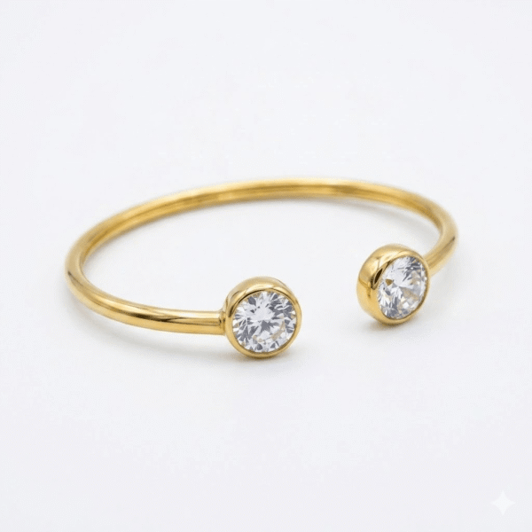 A slim, polished gold open-cuff kada featuring two round-cut bezel-set clear crystals on each end, displayed on a white background.