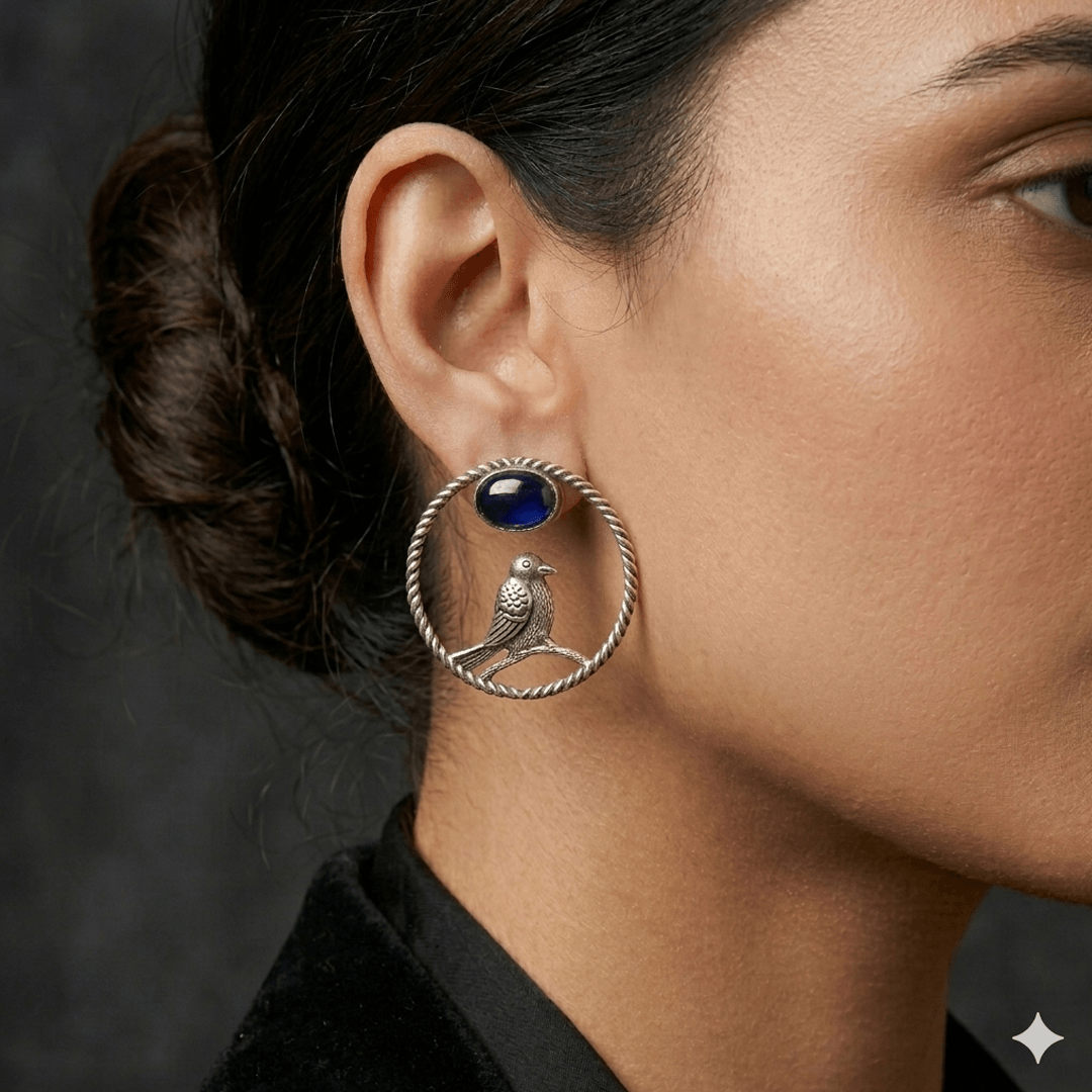 Woman wearing oxidised silver hoop earrings featuring bird motif and blue stone detailing.