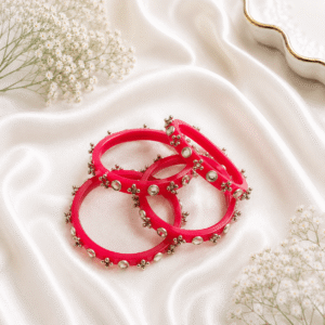 Bright pink designer bangles with stone embellishments and silver bead detailing displayed on white satin fabric.