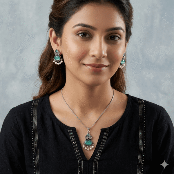 A young woman wearing a traditional oxidized silver necklace and earring set featuring green stones and pearl hangings on a black kurti.
