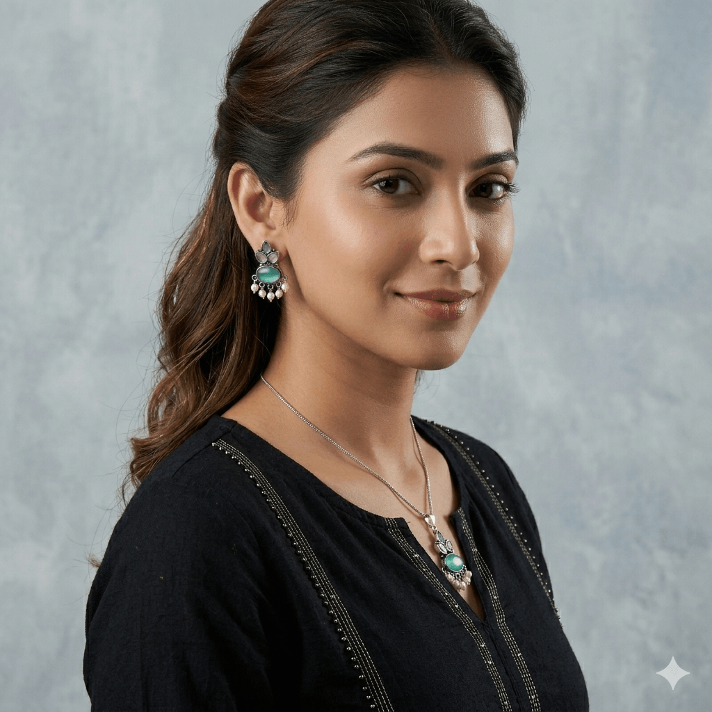 A young woman wearing a traditional oxidized silver necklace and earring set featuring green stones and pearl hangings on a black kurti.