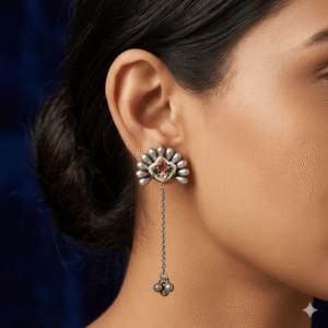 Woman wearing silver floral stud earrings with long chain drop and ghungroo detailing.