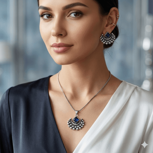 A high-resolution, square close-up of a elegant woman from the collarbone up, showcasing an intricate handcrafted oxidized silver crescent moon pendant with silver beads and a deep square-cut blue stone, suspended on a fine chain. She is also wearing the matching studded crescent moon earrings on her ear.