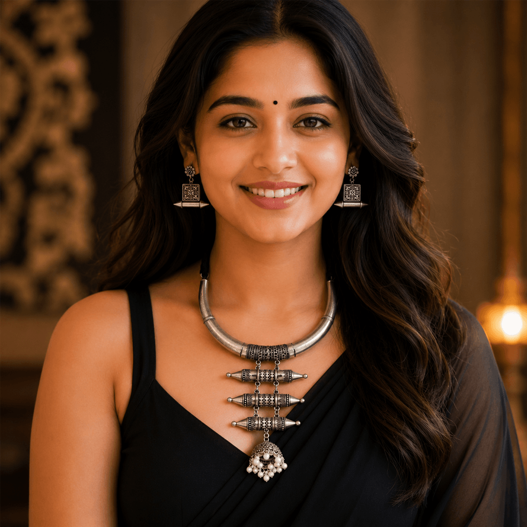 A model showcasing a Kreezo oxidized silver hasli necklace featuring a unique tiered spindle-style pendant with a pearl-drop jhumka, paired with matching square geometric earrings.