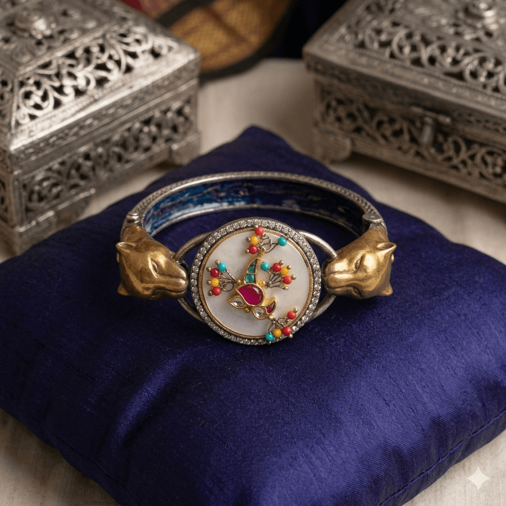 Modern Front view of a handcrafted silver and gold-plated leopard head bangle. The central feature is a circular mother of pearl dial with a detailed Kundan peacock design, surrounded by clear stones and flanked by two sculptural brass leopard heads on a dark blue patterned band.