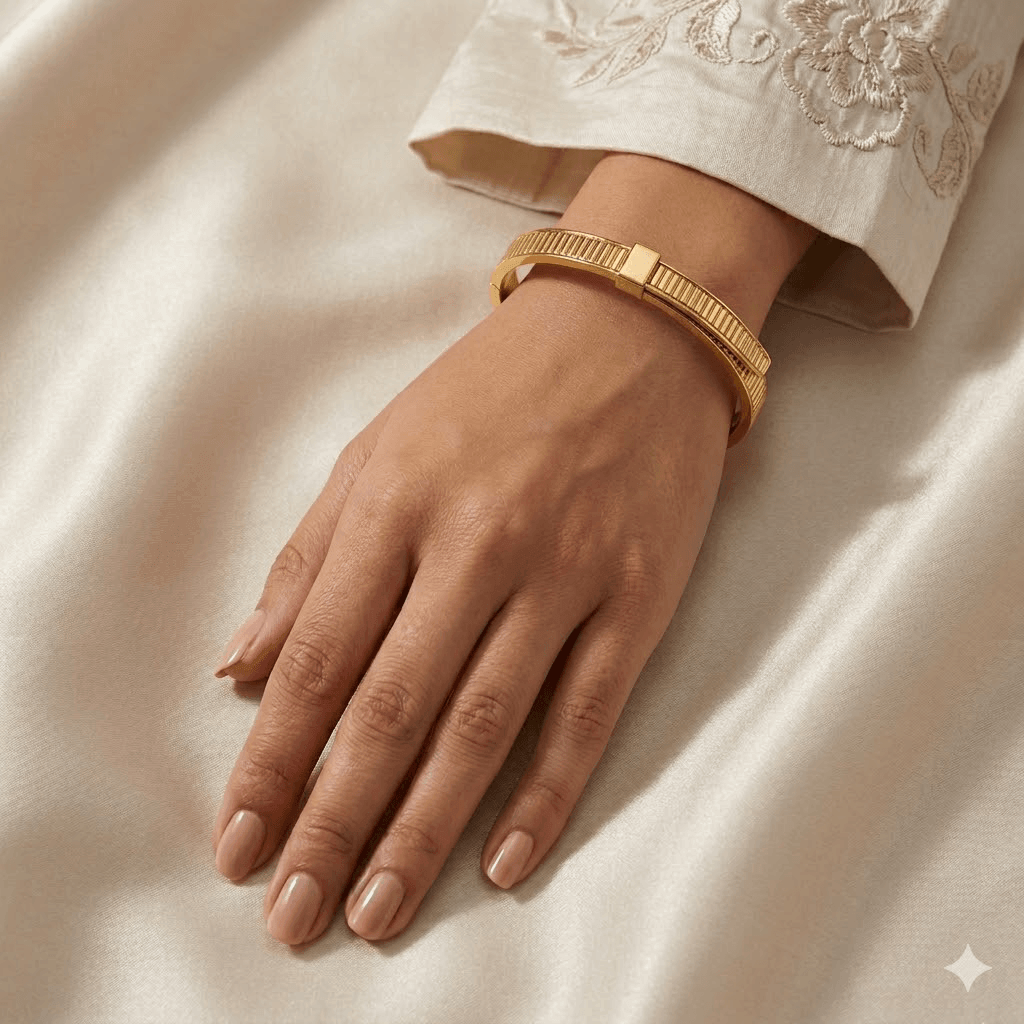 Model wear A polished yellow gold hinged bangle bracelet featuring a structured architectural ribbed pattern along the band, an asymmetric overlapping top closure with a central square clasp accent, and inner brand engravings.