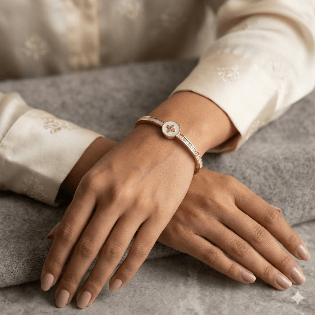 Model wear A slim, polished gold hinged kada featuring a central round medallion with an iridescent mother of pearl inlay and a gold four-petal floral monogram, flanked by a smooth mother-of-pearl band on one shoulder and a row of pave diamonds on the other.