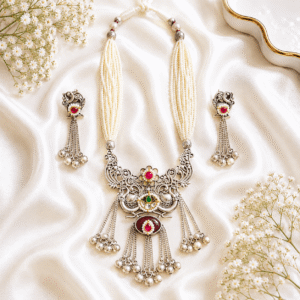 Elegant german silver necklace set with layered pearl strands, pink stone detailing, and matching tassel earrings displayed on white satin fabric.