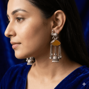 Model wear A pair of handcrafted German silver statement earrings featuring a detailed elephant motif at the top, a triangular amber-colored gemstone center, and hanging chain tassels with tiny silver bells and a small jhumka with pearl beads