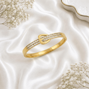 A sleek gold-plated bangle bracelet designed with a decorative buckle motif featuring two rows of clear cubic zirconia stones, resting on white satin fabric.