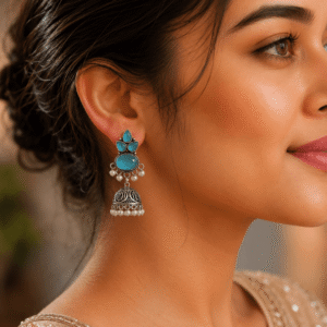 A woman wearing ornate silver-toned jhumka earrings featuring blue oval stones and delicate pearl accents.