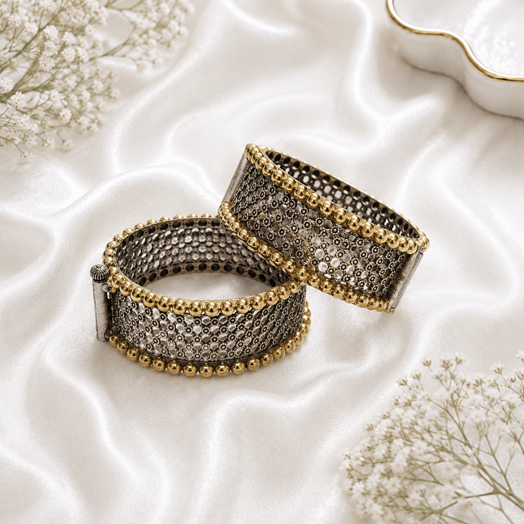 A pair of ornate dual-tone hinged bangles featuring a detailed silver filigree lattice pattern bordered by polished gold-tone bead work, displayed on white satin.