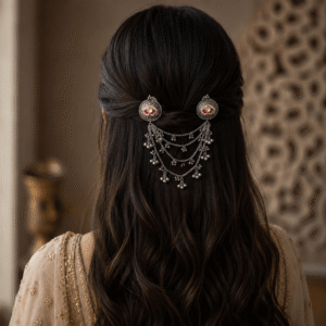 A woman with long dark wavy hair styled with two ornate German silver hair brooches connected by multiple tiers of delicate silver chains and small metallic dangles.