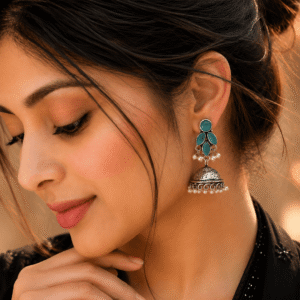 A woman wearing detailed German silver jhumka earrings adorned with turquoise-colored oval stones and delicate pearl bead accents.