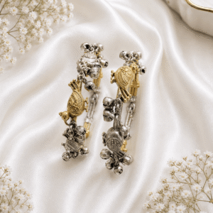 A pair of dual-tone silver and gold-plated Kada style bangles featuring intricate bird and tortoise charms with dangling silver ghungroo bells, displayed on a draped white satin background.