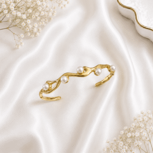 A gold-plated open cuff bracelet featuring an organic, fluid metal design adorned with four lustrous pearls, resting on white satin fabric.