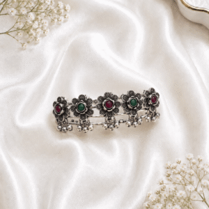 Oxidized silver kada bracelet with flower engraved panels, pink and green stones, and ghungroo bead detailing on white satin background