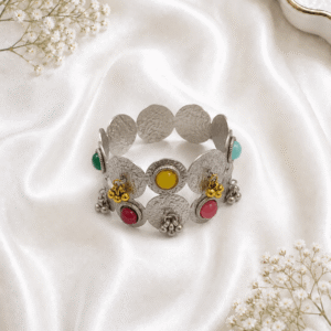 Oxidized silver kada bracelet with round disc design, multicolor stones, and hanging bead detailing on white satin background