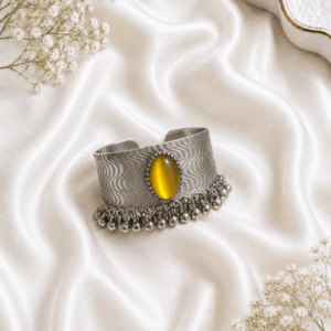 Oxidized silver kada bracelet with yellow stone and ghungroo bead detailing on white satin background