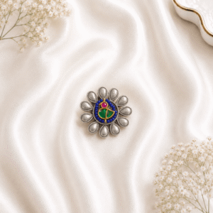 An ornate, circular oxidized silver ring featuring a stylized floral design with blue, green, and pink enamel detailing