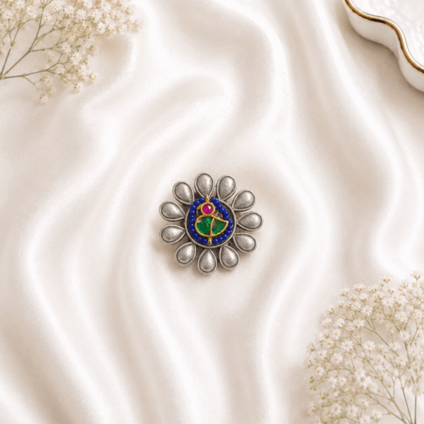An ornate, circular oxidized silver ring featuring a stylized floral design with blue, green, and pink enamel detailing