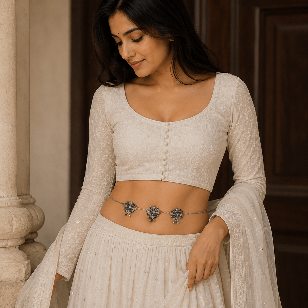 A woman wearing an all-white ethnic outfit adorned with an elegant, minimalist oxidized silver waist chain (Kandoro) featuring delicate floral motifs and small dangling beads.