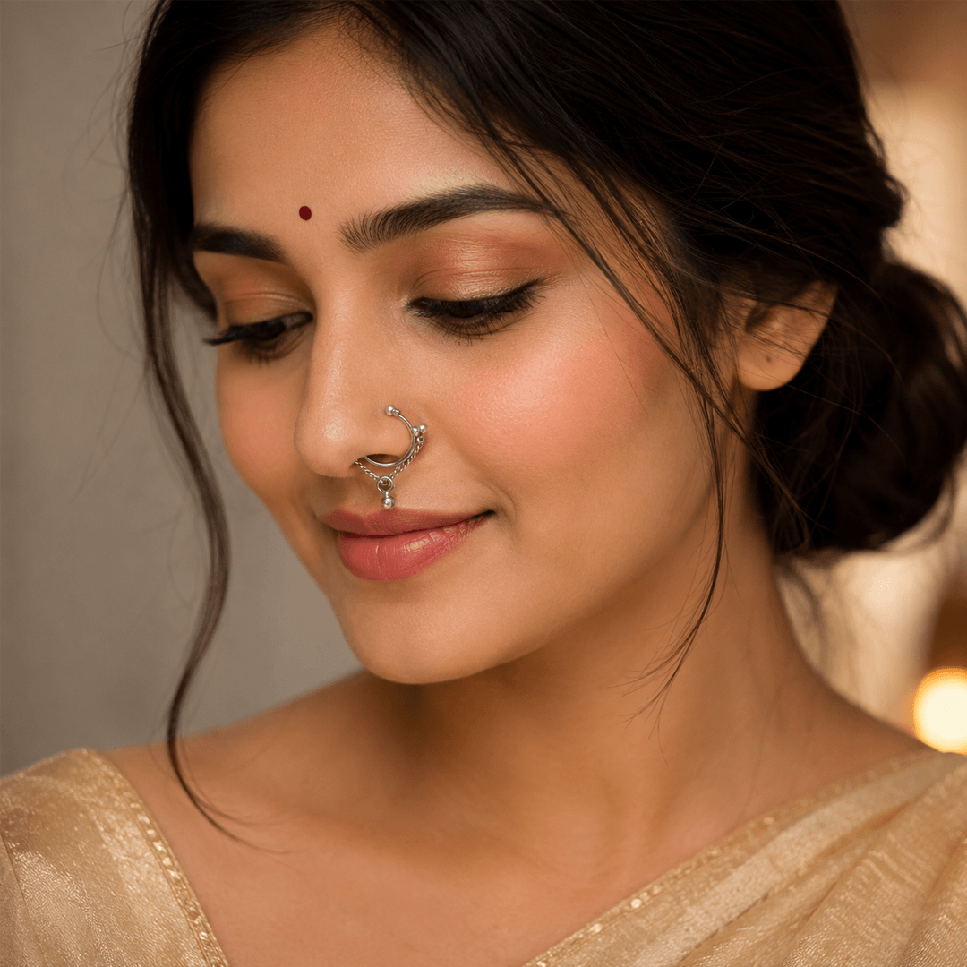 A close-up portrait of a woman wearing a simple, elegant silver hoop nose ring (Nath) featuring a thin chain connecting the top and bottom of the hoop with a small bead accent.