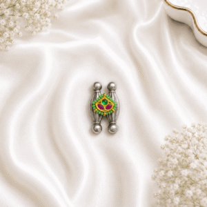 An artistic, tribal-inspired german silver ring featuring two vertical pillar-like structures centered with a vibrant gold-tone enamel motif adorned with green and pink stone accents, resting on white satin.