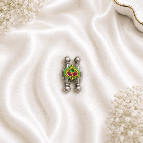 An artistic, tribal-inspired german silver ring featuring two vertical pillar-like structures centered with a vibrant gold-tone enamel motif adorned with green and pink stone accents, resting on white satin.