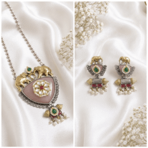 A premium antique silver jewelry set featuring a necklace and matching elephant motif earrings with pink stones, pearls, and green accents on a white silk background.