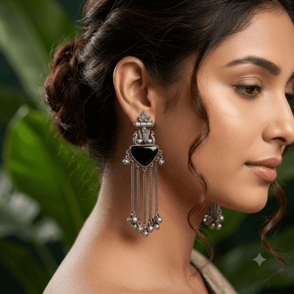 Close-up of a woman wearing premium German silver long tassel earrings featuring a black heart-shaped stone, antique detailing, and ghungroo accents.