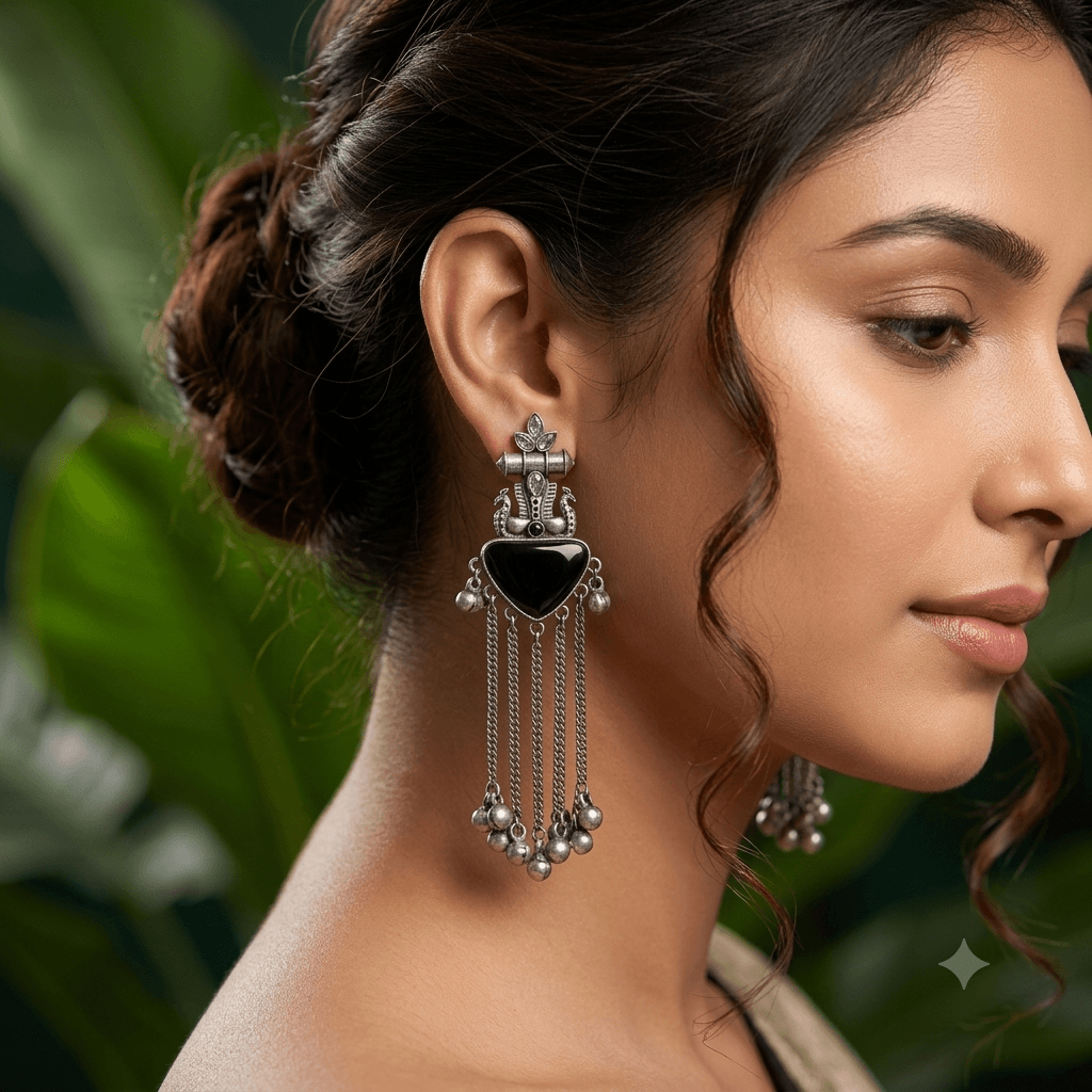 Close-up of a woman wearing premium German silver long tassel earrings featuring a black heart-shaped stone, antique detailing, and ghungroo accents.