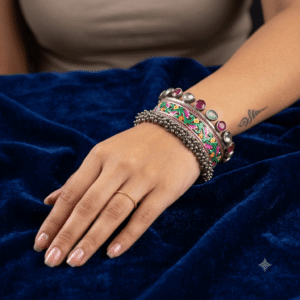 Hand wearing an oxidized silver kada bracelet featuring green marquise stones, mirror accents, and ghungroo bead detailing.