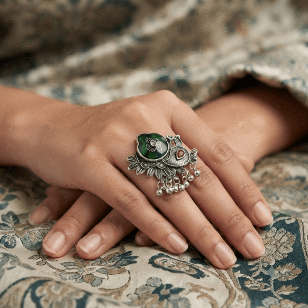Elegant oxidised silver peacock design adjustable statement ring with green enamel and dangling bead details worn on a woman's finger.
