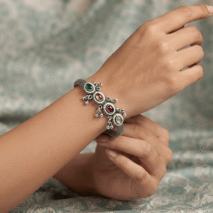 Woman wearing an oxidised silver adjustable kada bracelet with multicolor stone floral charms and traditional ethnic design.
