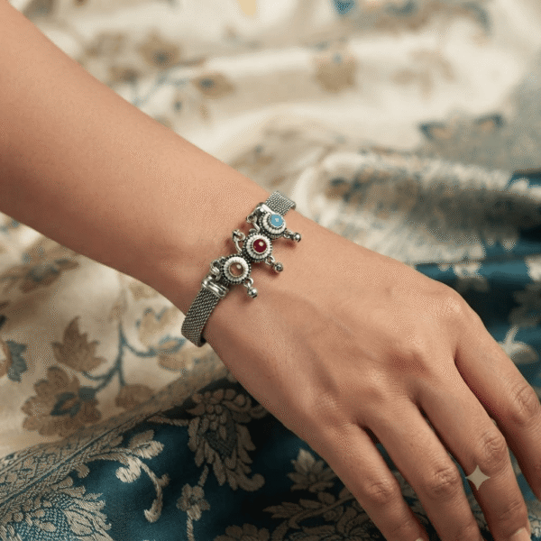 Woman wearing an oxidised silver adjustable kada bracelet with multicolor stone floral charms and traditional ethnic design.