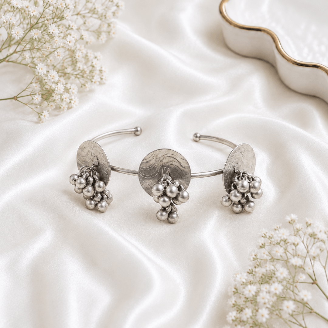 Oxidised silver kada bracelet with round disc design, dangling ghungroo beads and antique finish displayed on satin background.