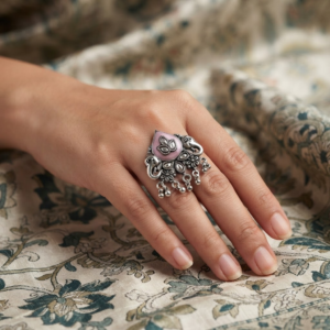 Woman wearing an oxidised silver adjustable statement ring with pink stone, peacock design, floral detailing, and ghungroo charms.