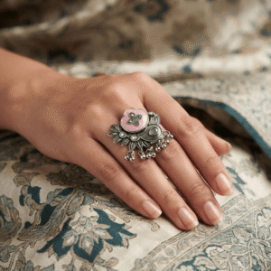 Woman wearing an oxidised silver statement ring with pink stone, floral detailing, leaf motif, and ghungroo charms.