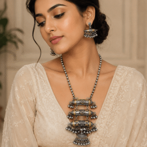 A model wearing a sophisticated dual-tone oxidized silver necklace with matching drop earrings, featuring ethnic cylindrical motifs and ghungroo-style beads.