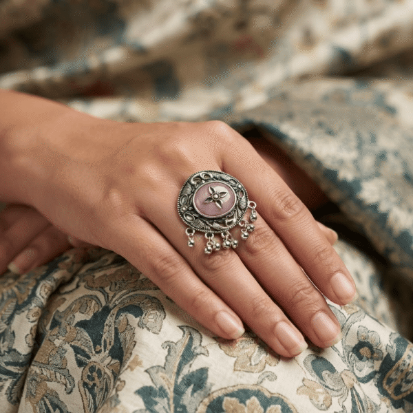Premium close-up of a woman wearing an oxidized German silver floral statement ring with a pink stone and hanging ghungroo detailing.