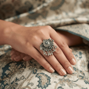 Premium close-up of a woman wearing an oxidized German silver floral statement ring with a green stone, intricate antique detailing, and hanging ghungroo charms.