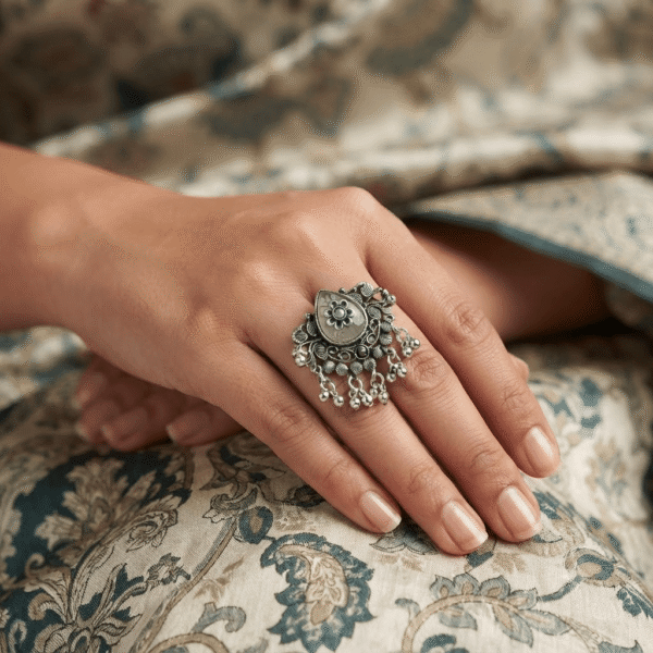 Premium close-up of a woman wearing an oxidized German silver floral statement ring with a green stone, intricate antique detailing, and hanging ghungroo charms.